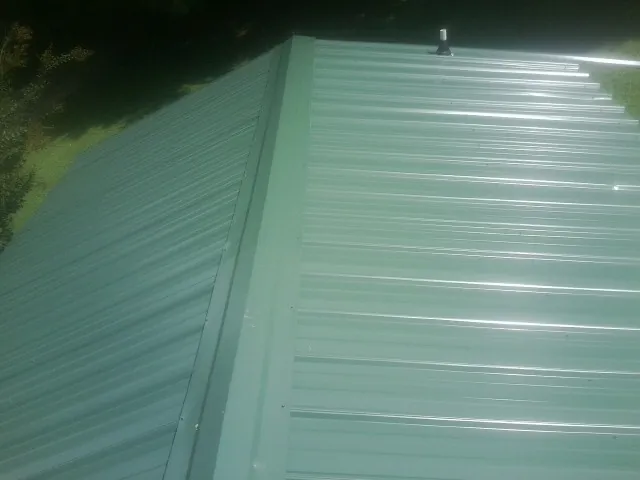New green metal panels meeting at the ridge of a roof — Flat Roof Repair work by our crew in Girard